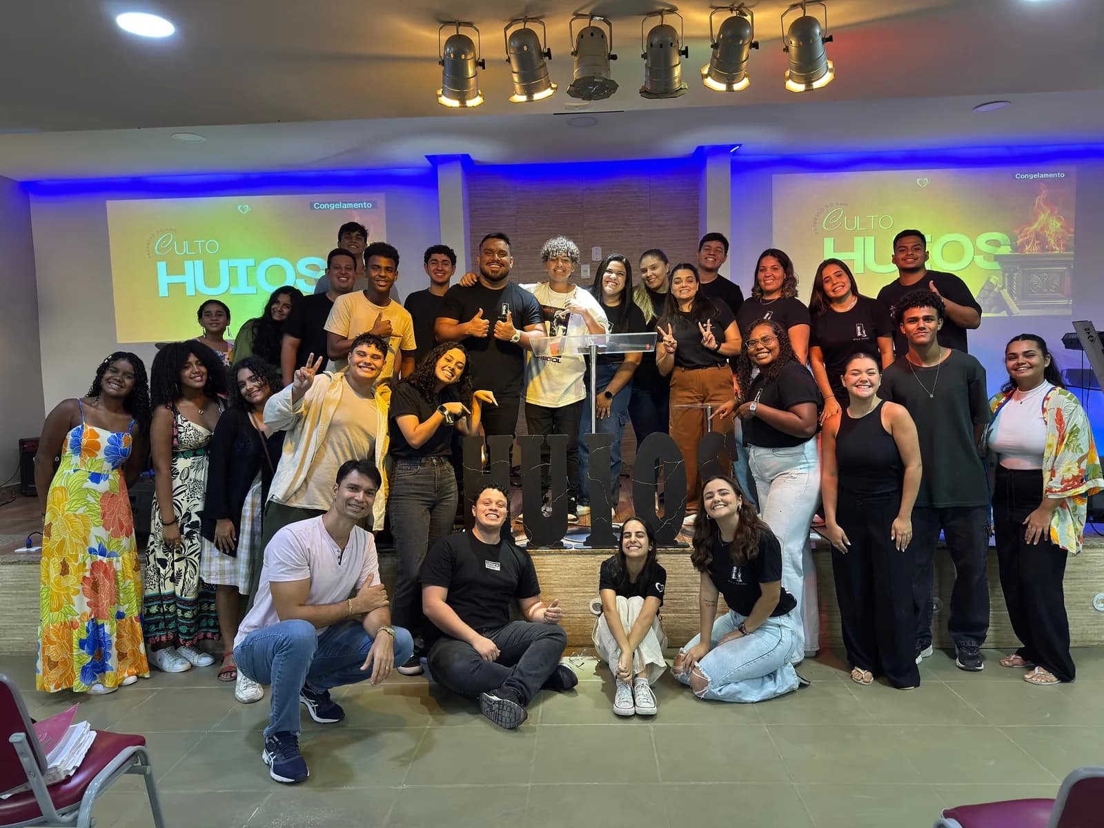 Grupo grande de jovens reunidos no palco em uma noite do Huios