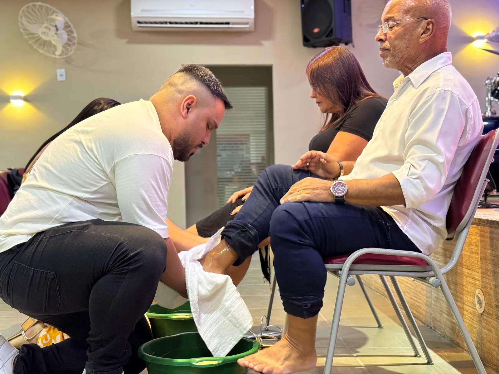 Homem ajoelhado lavando os pés de uma irmã durante o culto