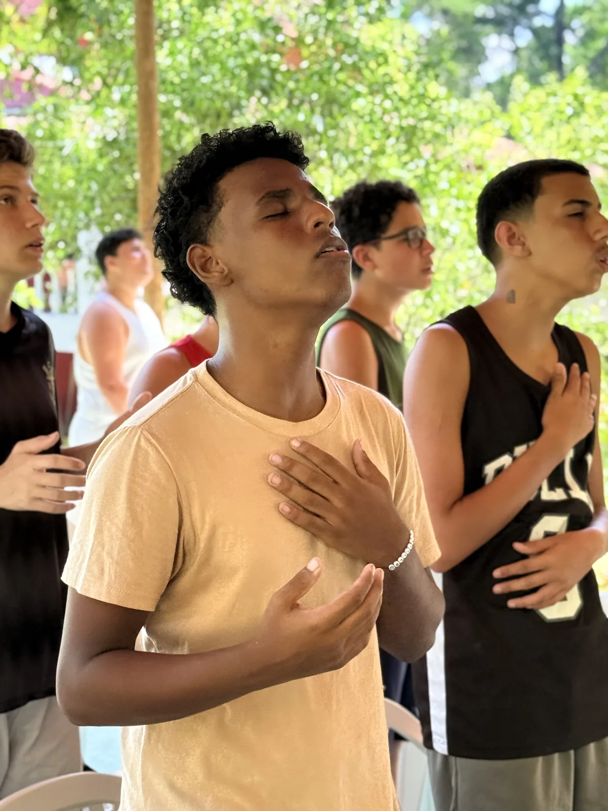 Jovens do Retiro Huios em adoração ao ar livre, mão sobre o peito
